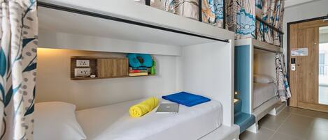 A bunk bed room with a shelf above the lower bunk holding books and a power outlet.