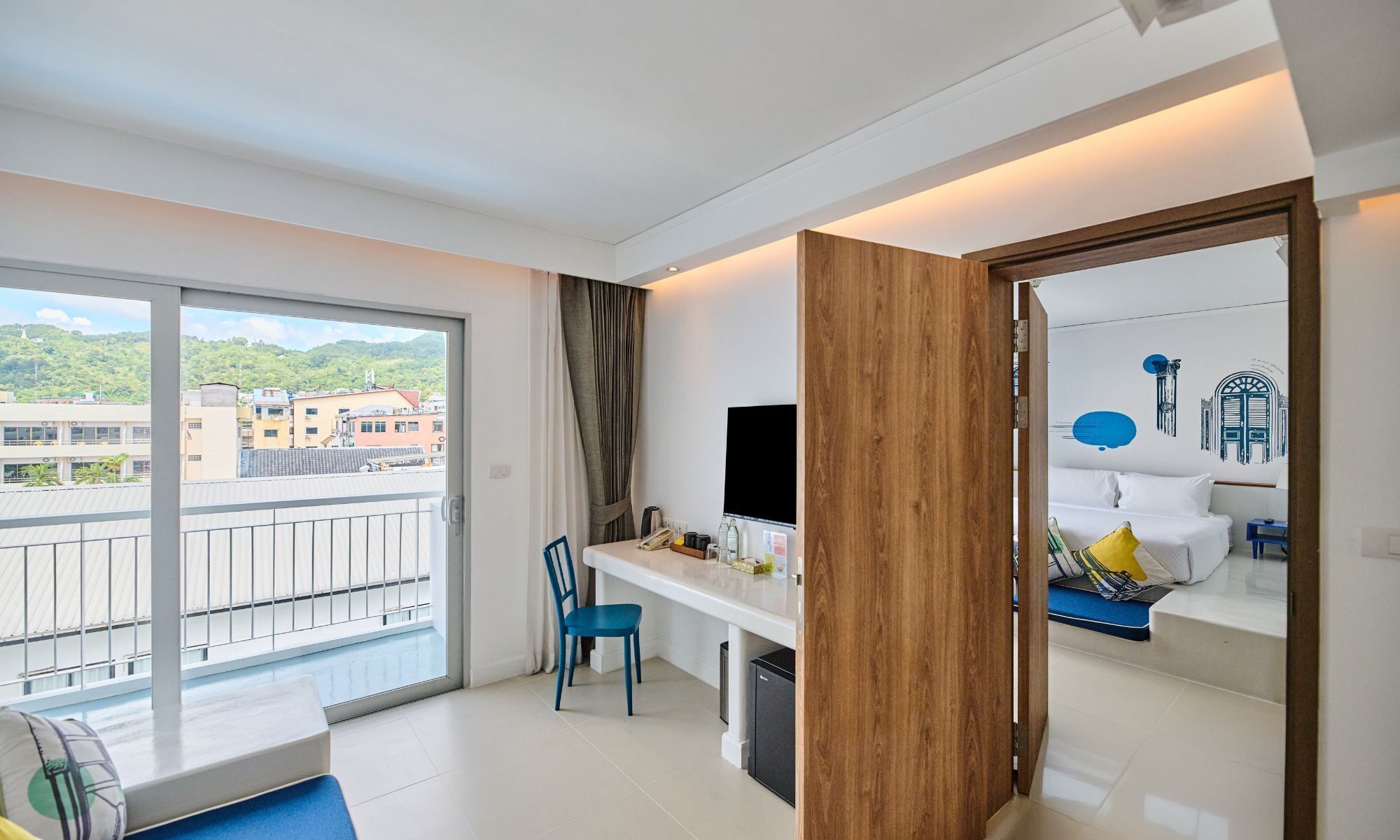 Ein Hotelzimmer mit Balkon, Schreibtisch mit Stuhl, Bett und Fernseher.