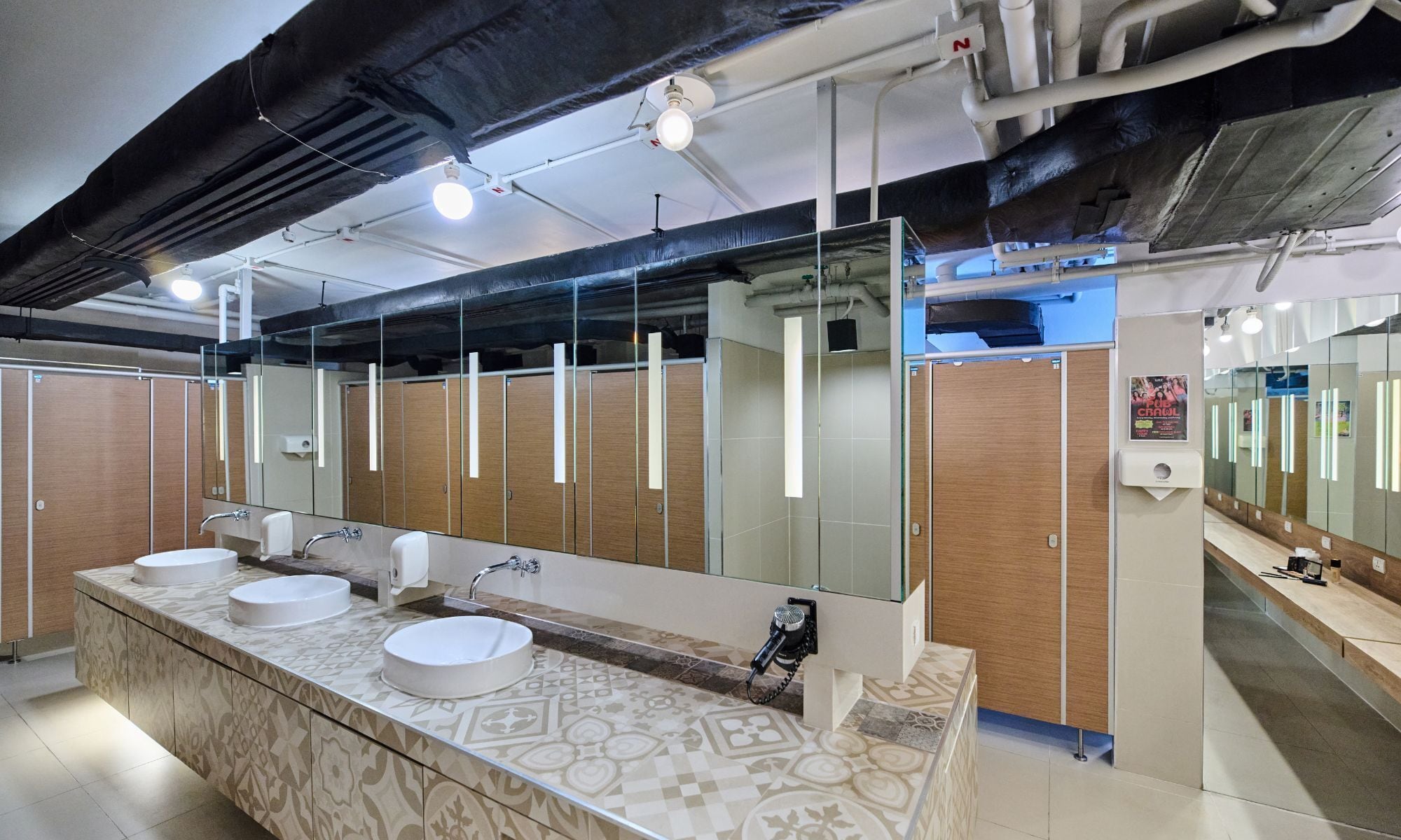 A modern restroom with two sinks, a large mirror, and wooden partitions.