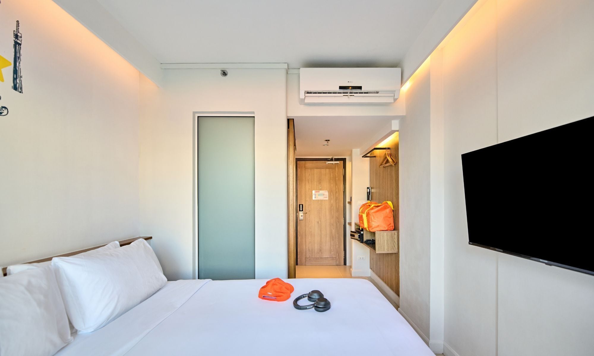 A hotel room with a bed, a TV, and an air conditioning unit.