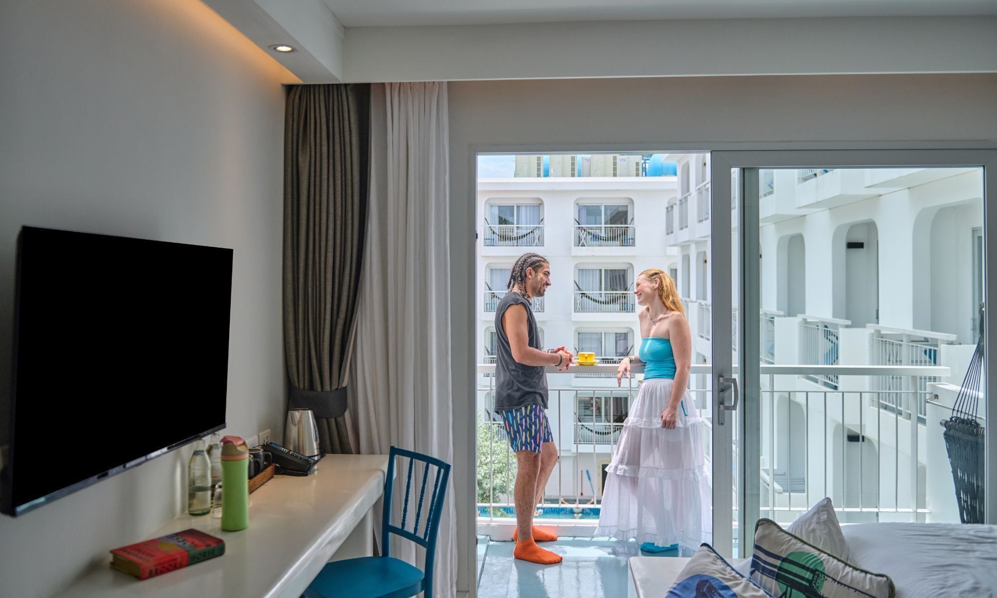 Una habitación de hotel con balcón, televisión, escritorio con silla y cama.