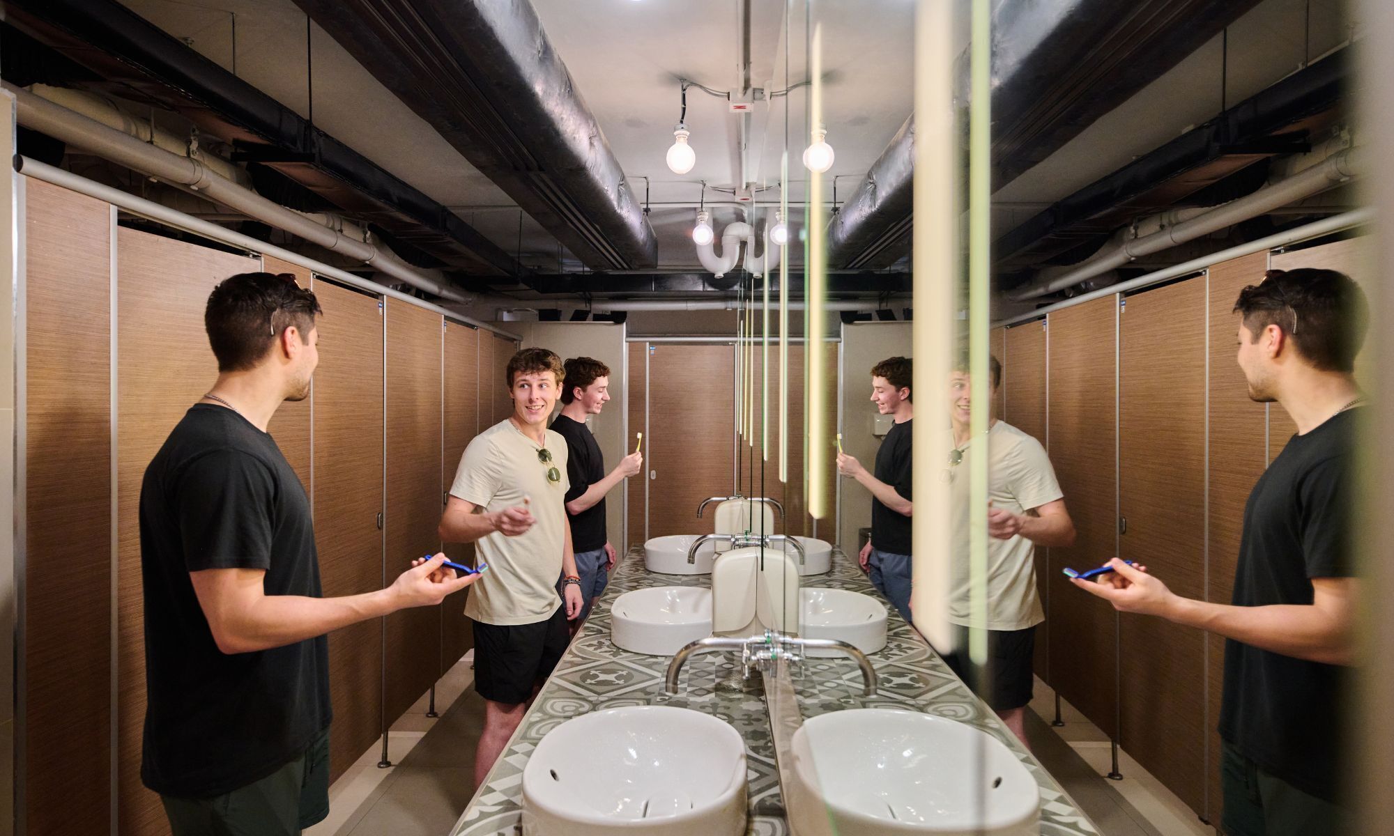 A modern bathroom with multiple sinks, wooden lockers, and overhead lighting.
