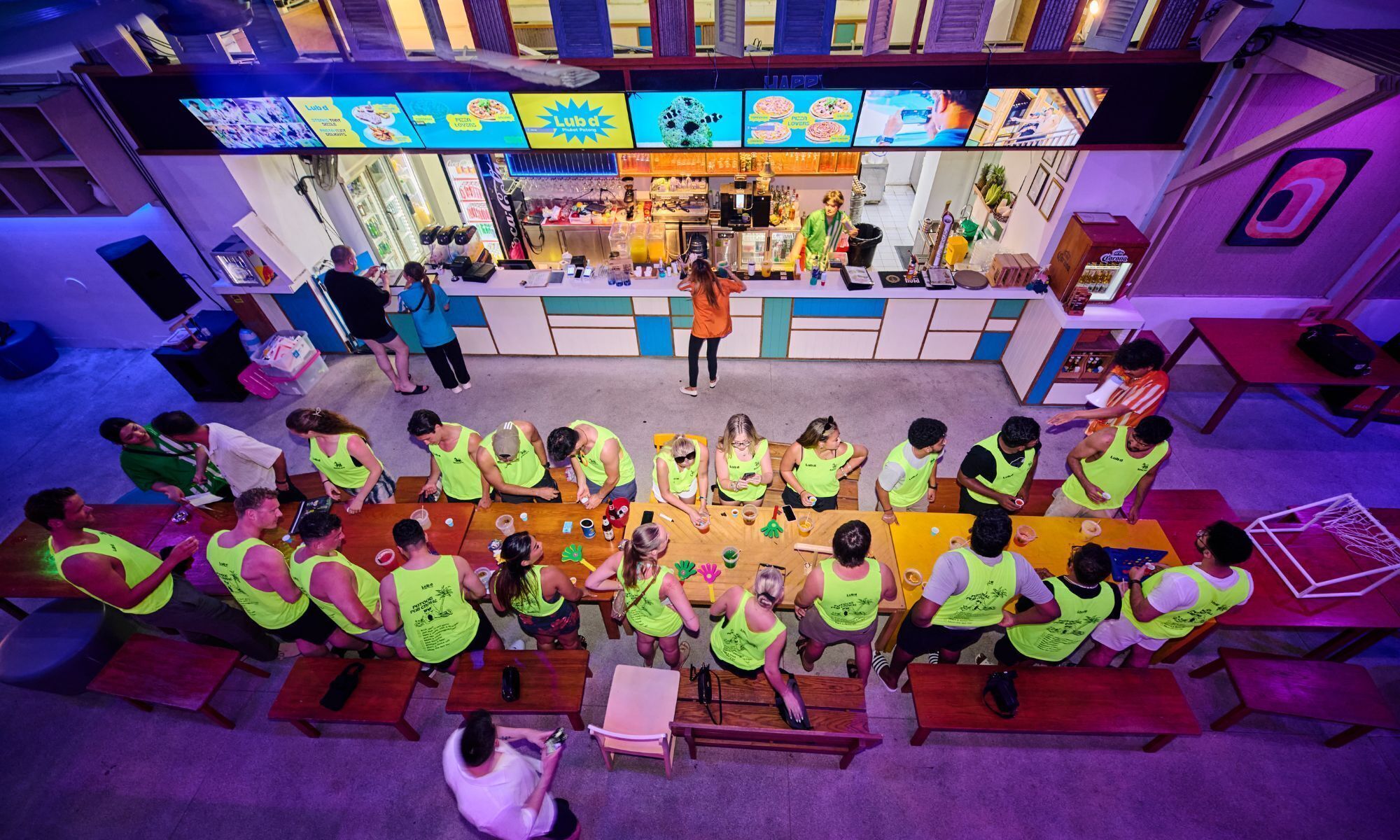 A group of people in a brightly lit indoor space with tables and chairs arranged in a semi-circle.