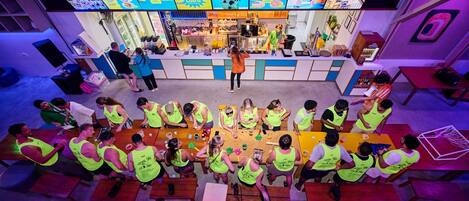 A group of people in a brightly lit indoor space with tables and chairs arranged in a semi-circle.