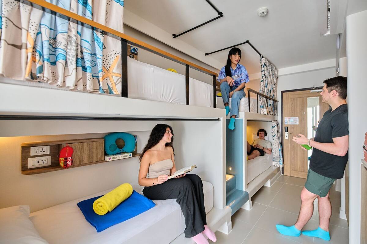 A dormitory-style room with bunk beds, a small desk, and a window with curtains.