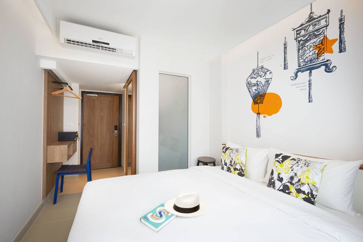 A hotel room with a bed, a desk, a chair, and a wardrobe.
