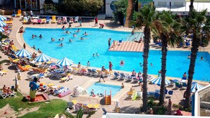 A large swimming pool surrounded by sun loungers and umbrellas, with palm trees and a building in the background. - Eden Club Skanes (Monastir)