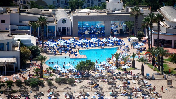 A resort with a large swimming pool surrounded by numerous sun loungers and umbrellas, a sandy beach area with beach chairs and umbrellas, and a building with a dome structure. - Eden Club Skanes (Monastir)