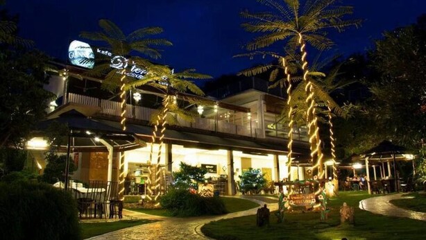 A hotel with a covered outdoor area, palm trees, and a sign that reads "Gunn's Cafe." - Laman Pesona Resort & Spa (Raub)
