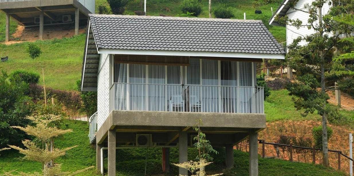 Una casa de dos pisos con balcón, rodeada de vegetación.
