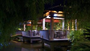 A gazebo with a wooden deck and railing, surrounded by lush greenery and a body of water. - Laman Pesona Resort & Spa (Raub)