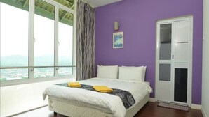 A bedroom with a large window, a bed with white bedding, a purple wall, and a door with a glass panel. - Laman Pesona Resort & Spa (Raub)