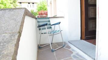 Una silla con un cojín a rayas apoyada contra una pared blanca, un repisa de piedra y una puerta con un panel de vidrio.