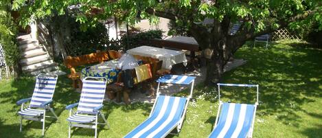Un patio con sillones de descanso, una mesa y una zona de barbacoa bajo un árbol.