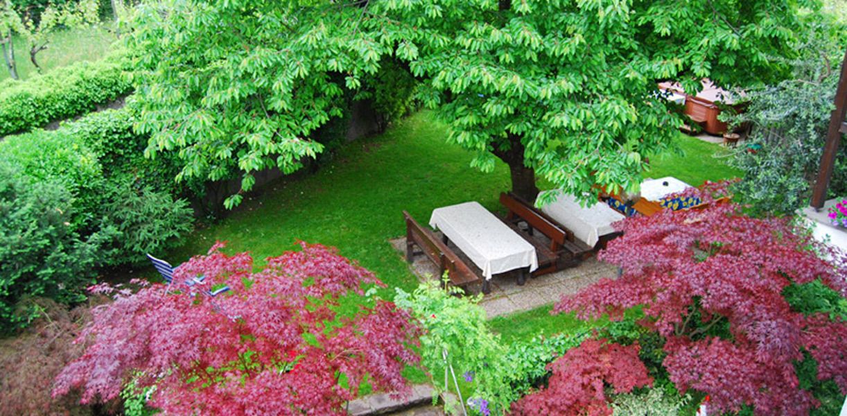 Ein Garten mit Picknicktisch und Bänken, umgeben von üppigem Grün und blühenden Pflanzen.