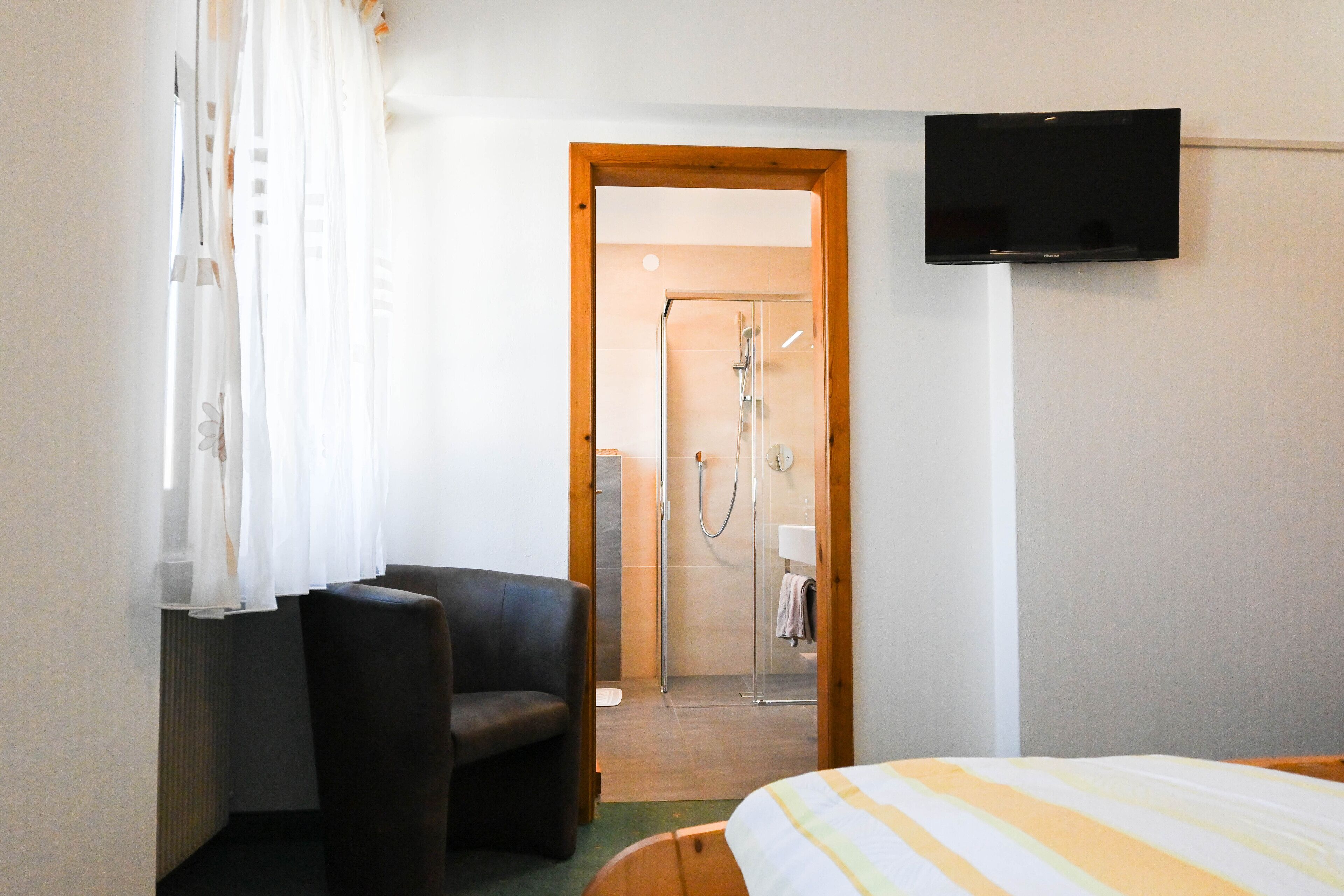 Ein Hotelzimmer mit Bett, Stuhl, Fernseher und Duschbereich.