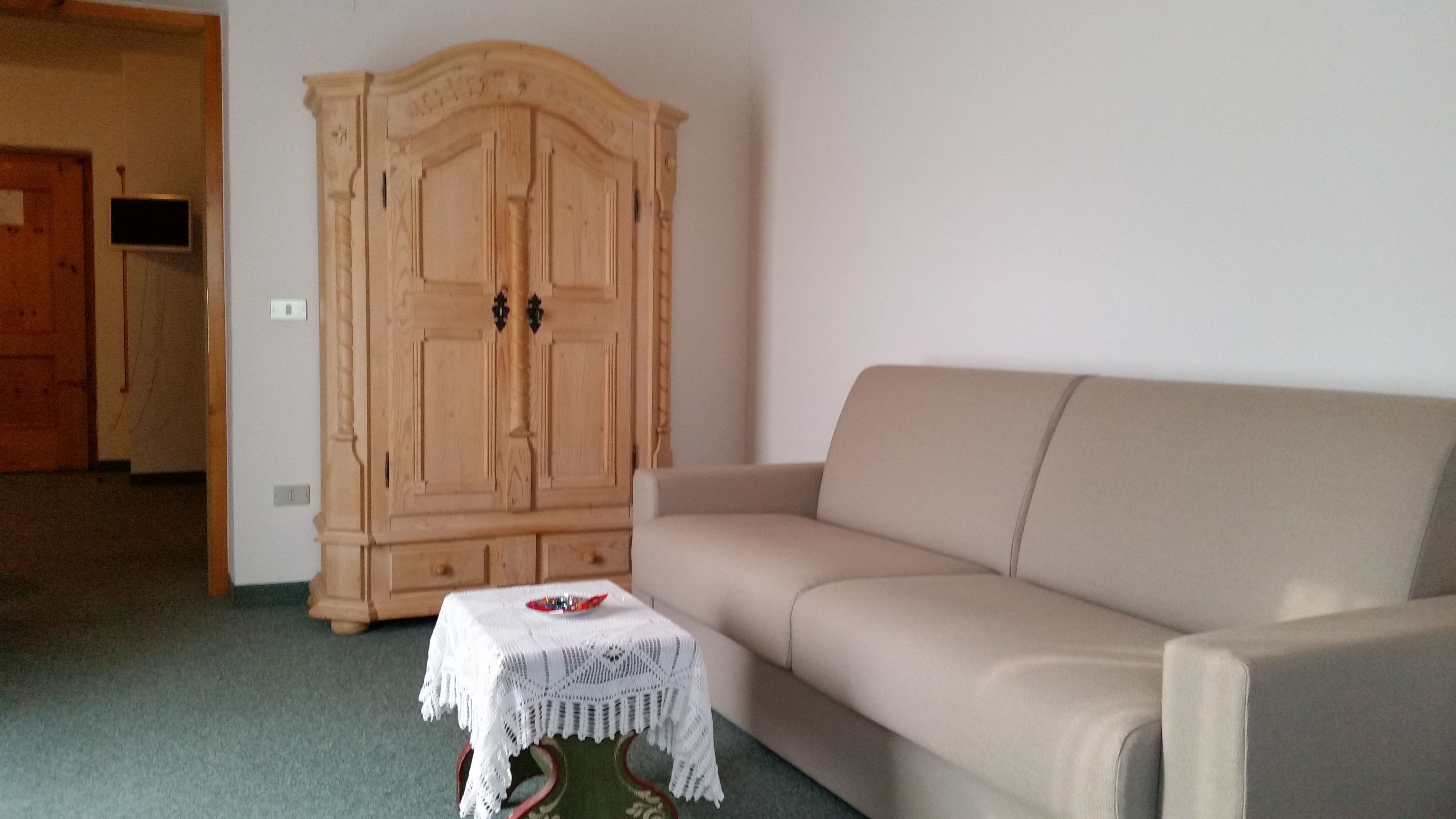 A living room with a beige sofa, a wooden cabinet, and a small white table with a red object on it.
