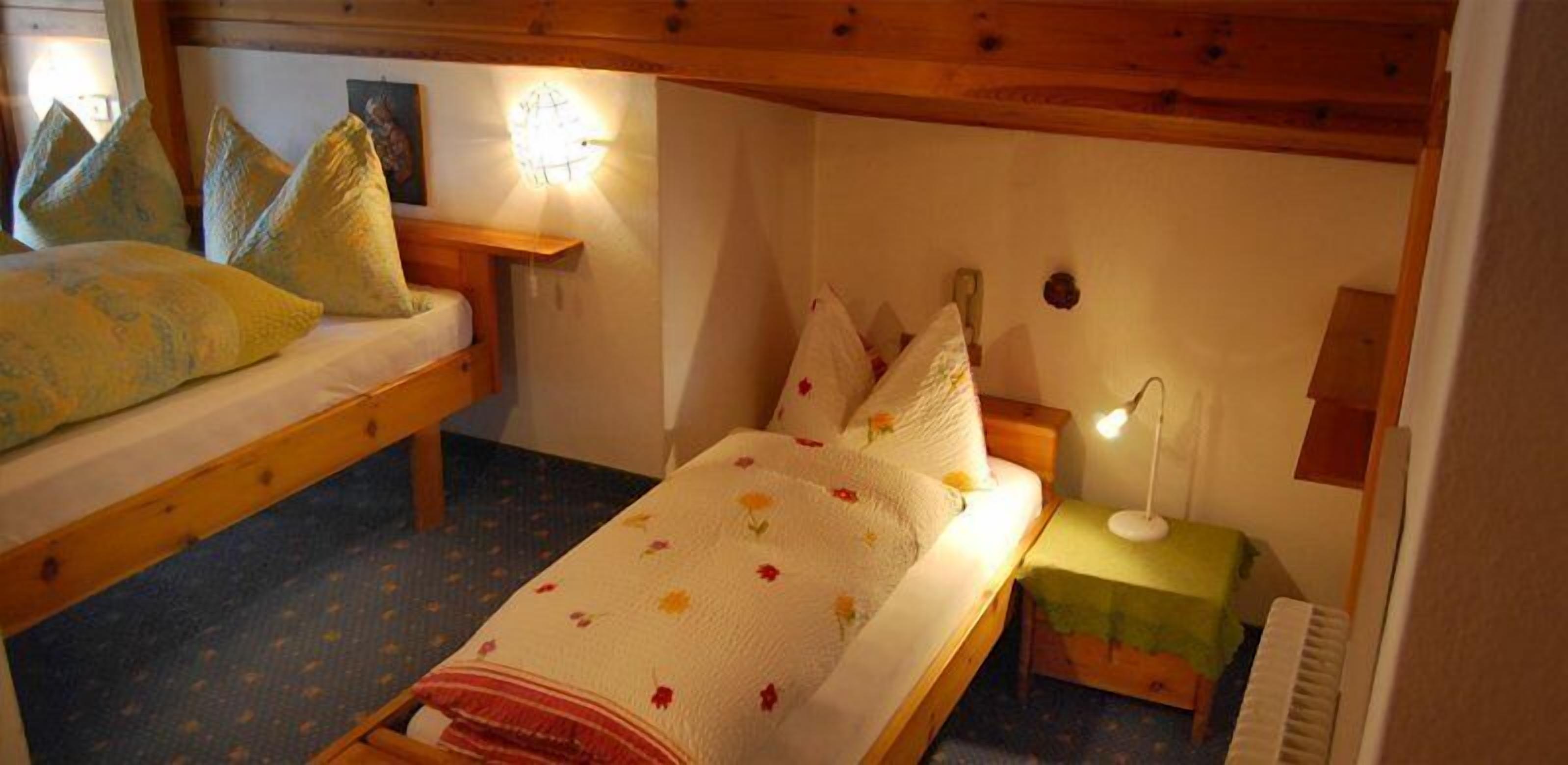 Una habitación acogedora con dos camas de madera, una mesita pequeña y una mesita de noche con lámpara.