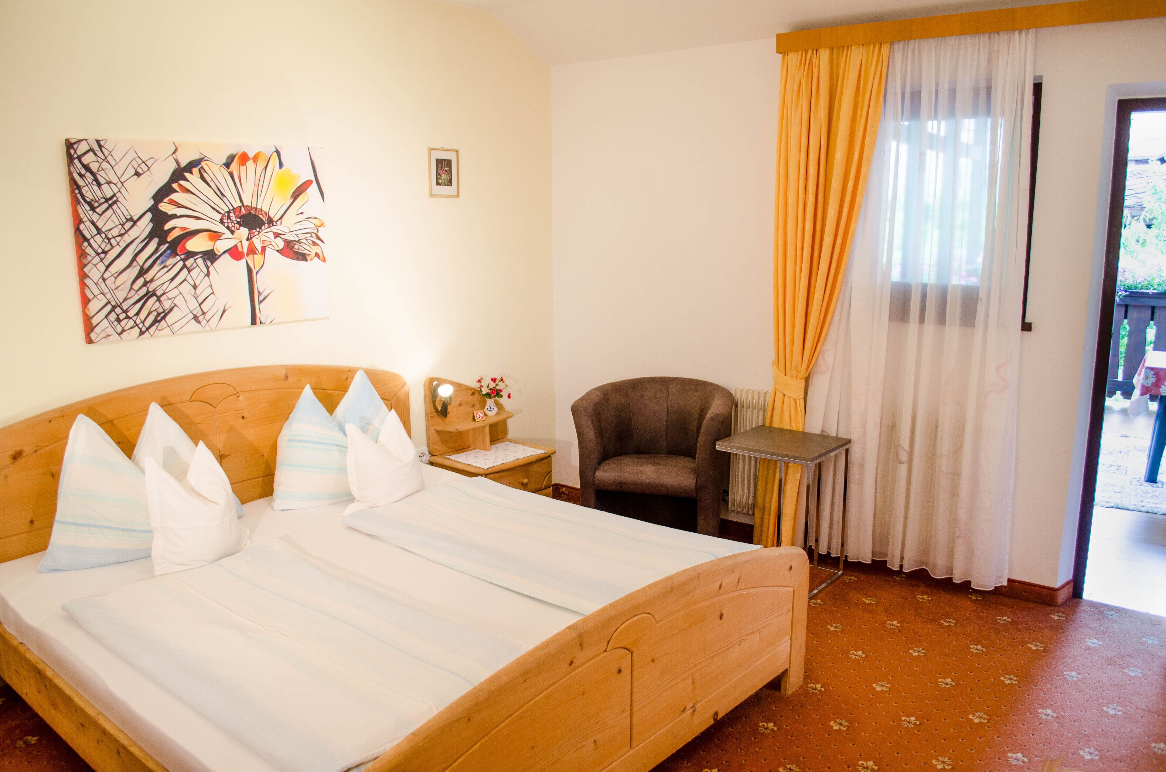 Une chambre à coucher avec un lit en bois, une chaise, une petite table et une fenêtre avec des rideaux.