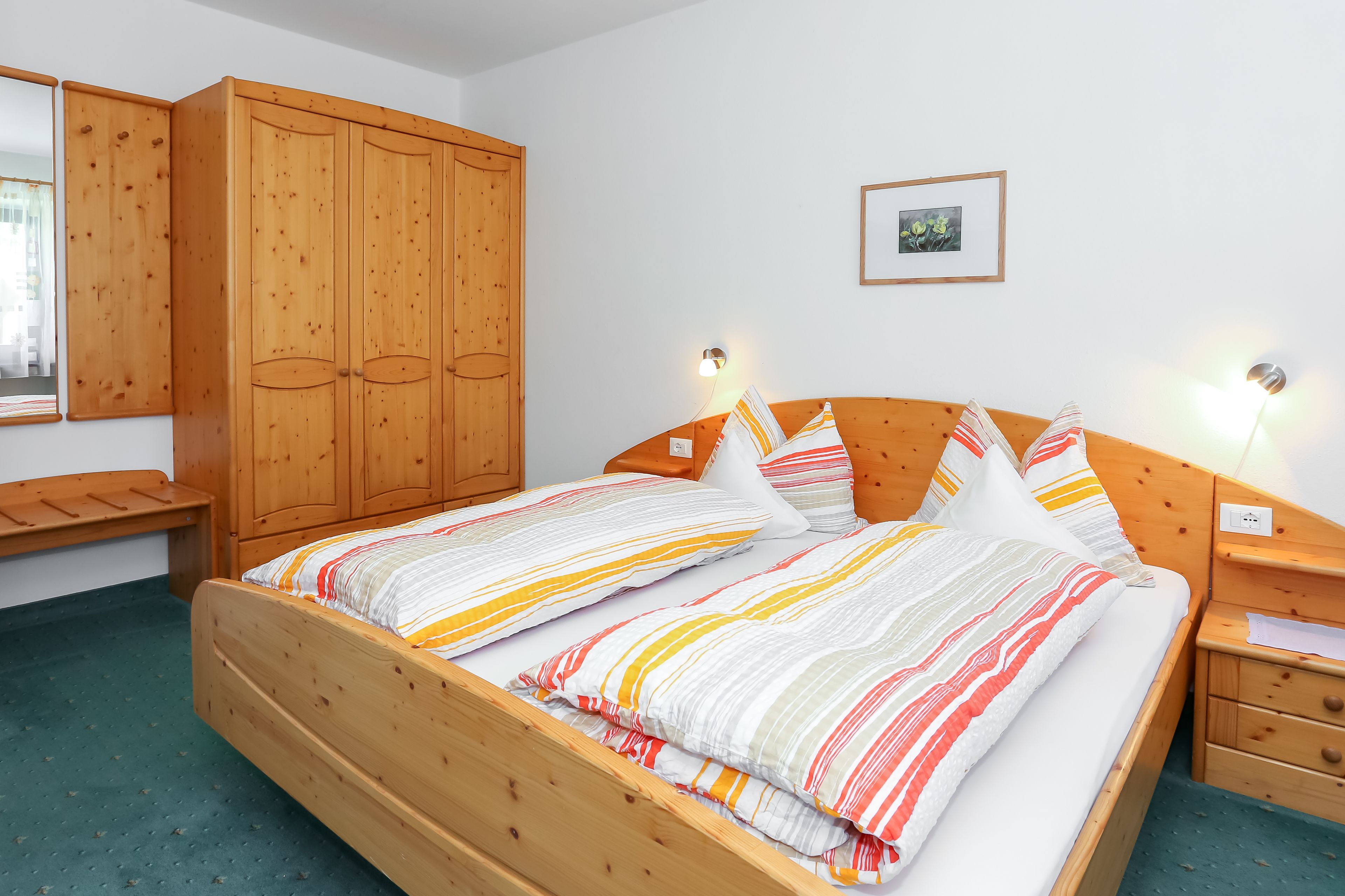 Uma cama de madeira com roupa de cama listrada, um guarda-roupa de madeira e uma mesa de cabeceira com uma lâmpada.