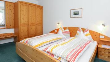 Uma cama de madeira com roupa de cama listrada, um guarda-roupa de madeira e uma mesa de cabeceira com uma lâmpada.