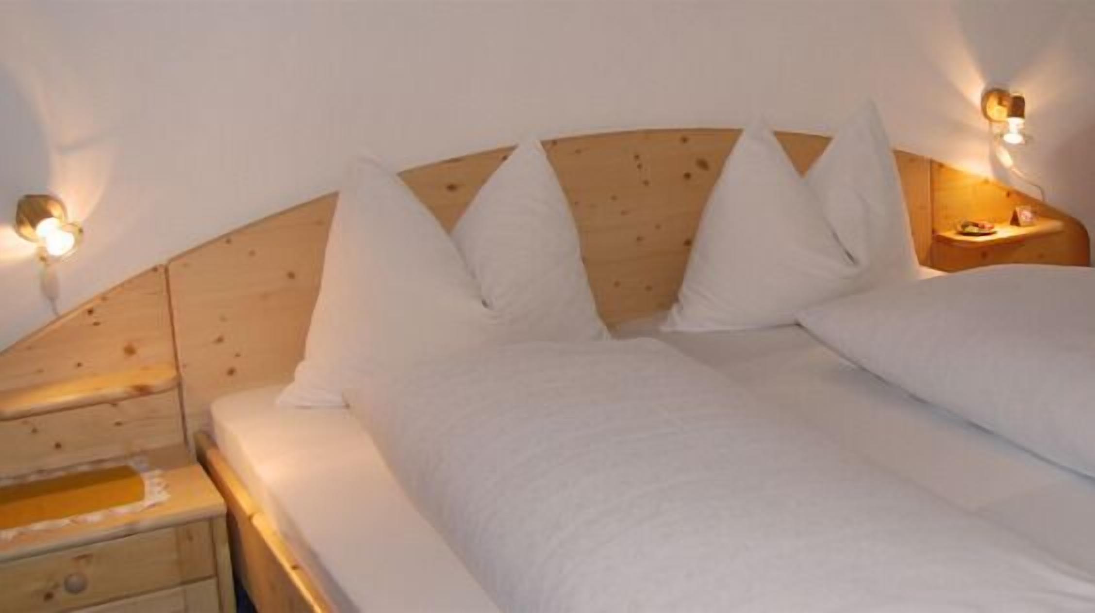 Un dormitorio con cabecera de madera, ropa de cama blanca y dos mesitas de noche con lámparas.