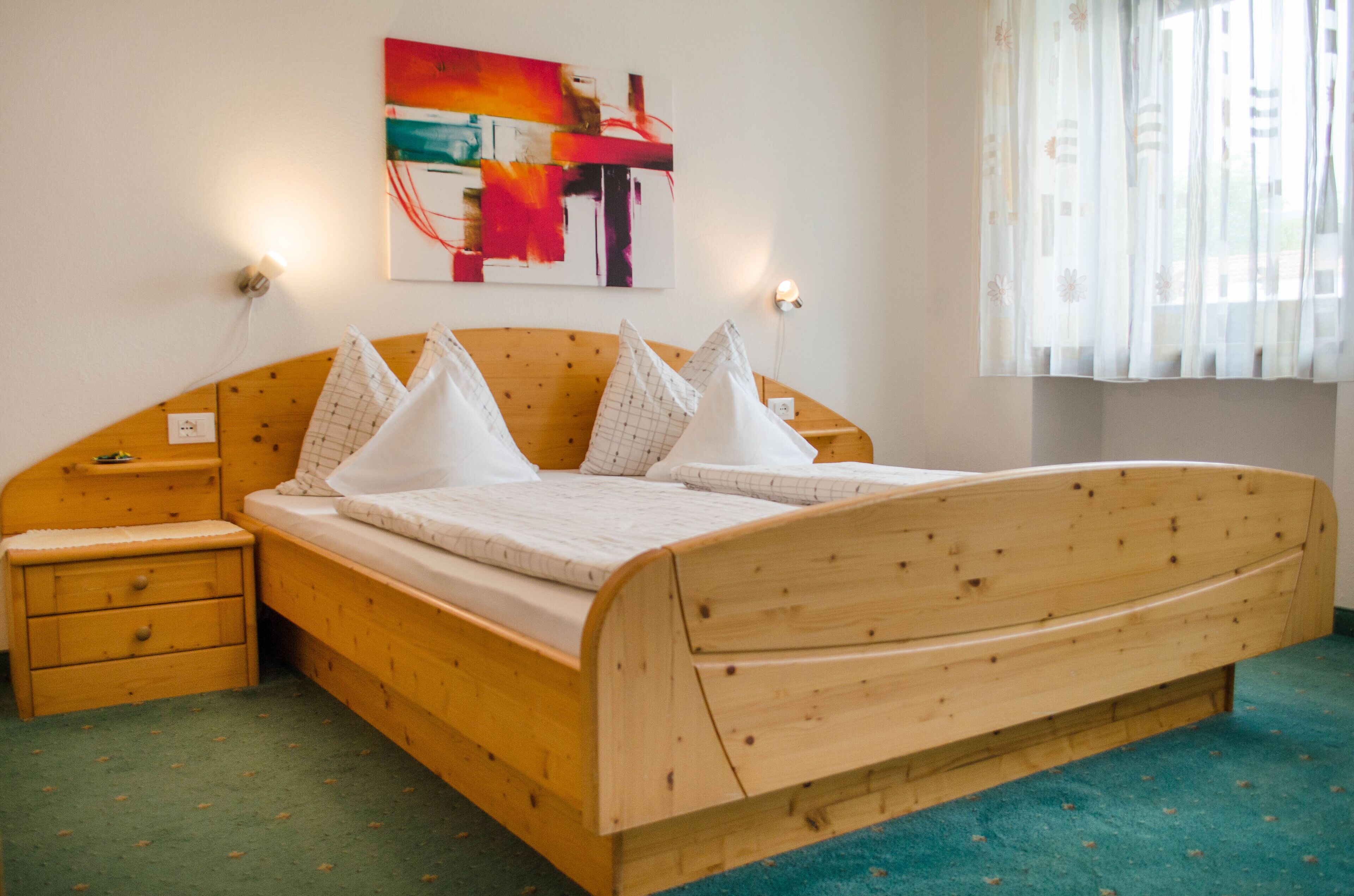 Een houten bed met hoofdeinde, twee nachtkastjes en een aan de muur hangend schilderij.