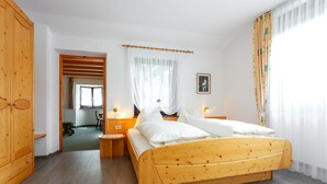 A wooden bed with white bedding, a wooden wardrobe, and a bedside table with a lamp. - Garni Meinrad (Ora)