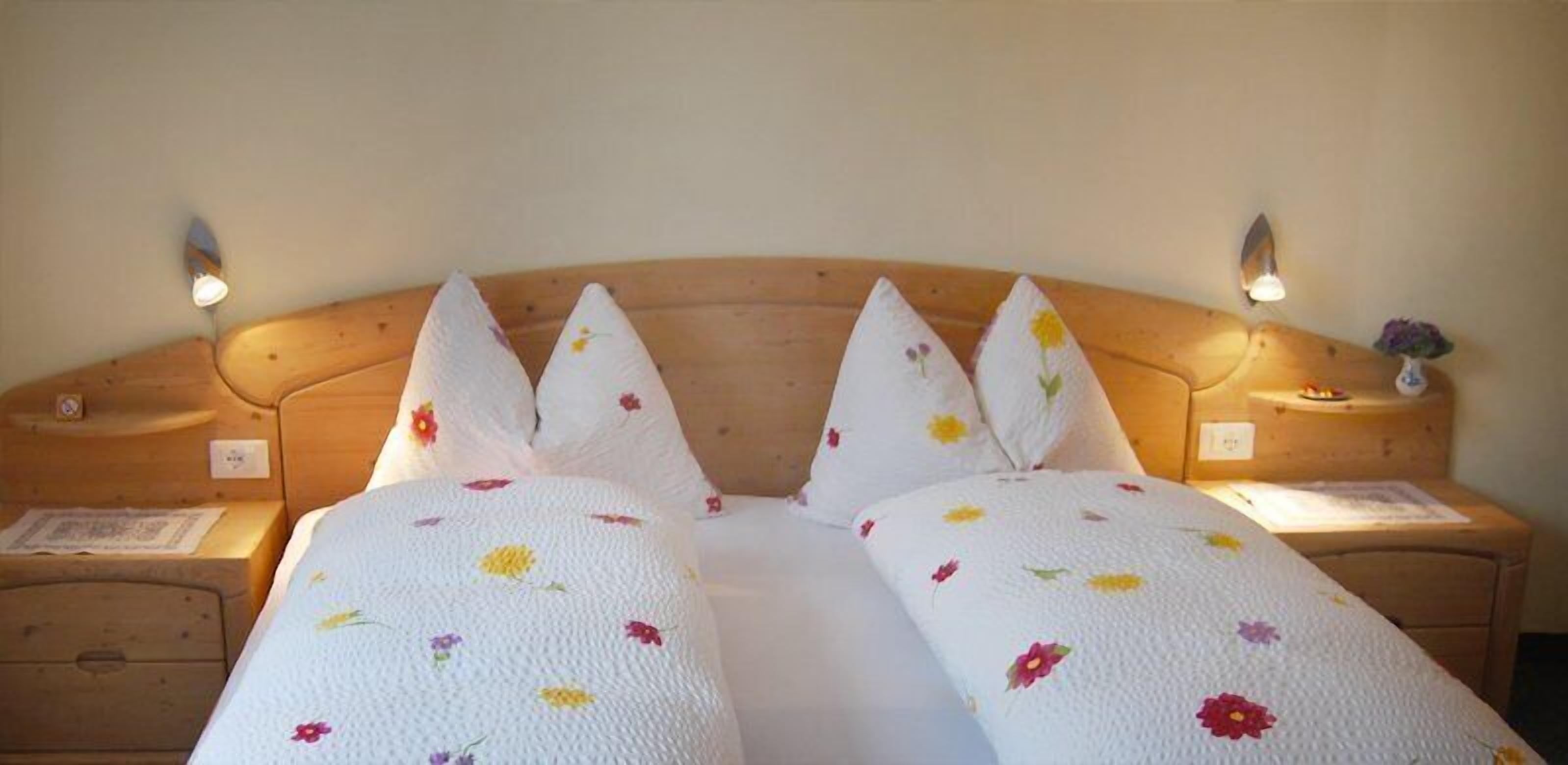 Ein Doppelbett mit floralem Bettbezug, zwei Nachttische mit Lampen und ein Holzkopfstück.