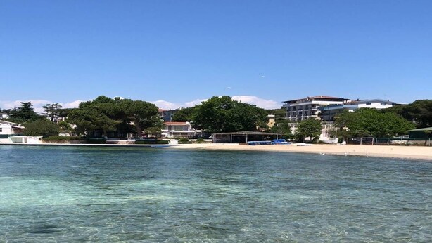 A clear beach with a sandy shore and buildings in the background. - Paradise Island Hotel (Darica)