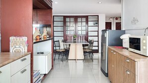 Een kleine keuken met een eettafel, stoelen, een magnetron en een koelkast.