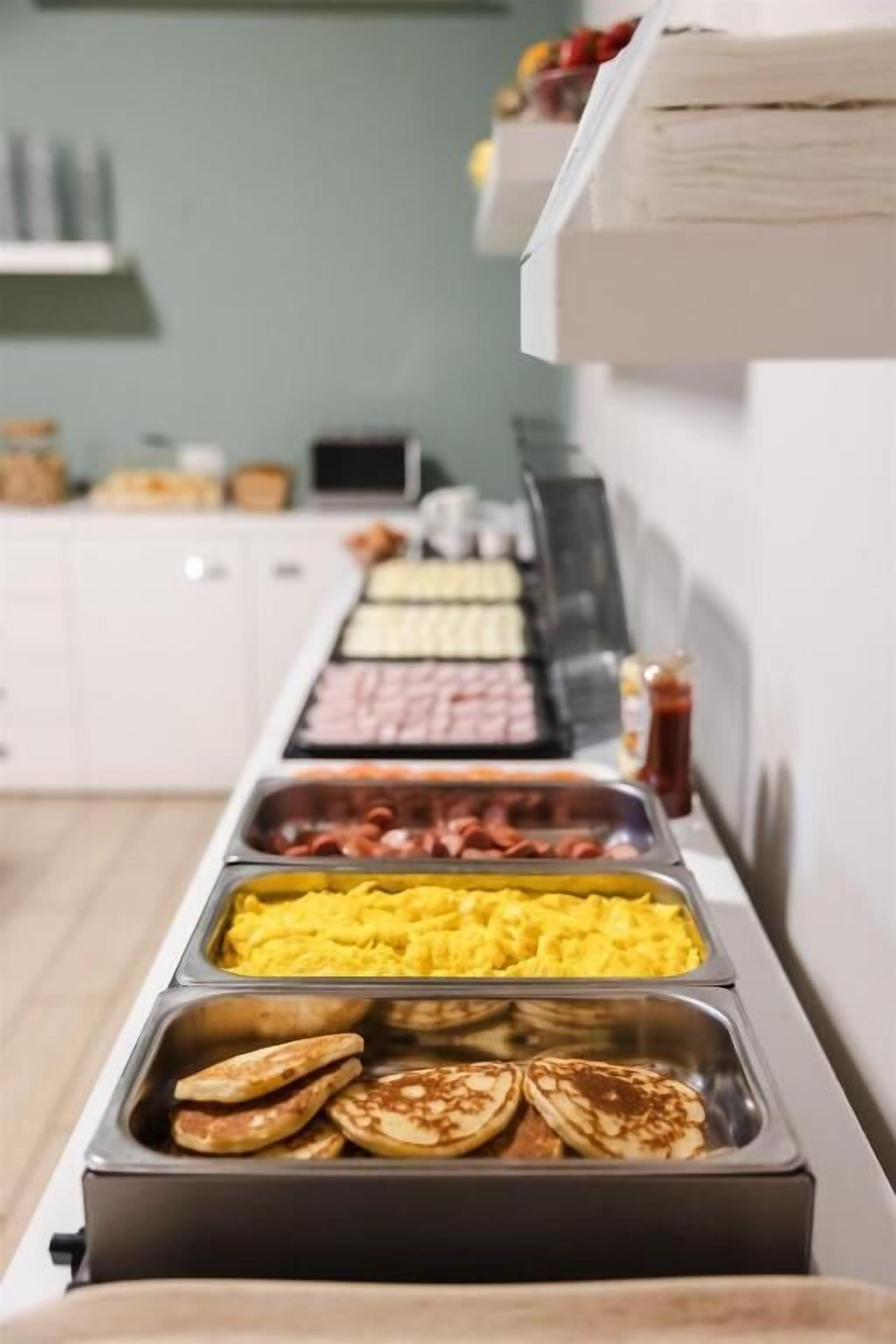 A buffet with various food options including scrambled eggs, sausages, and pancakes.