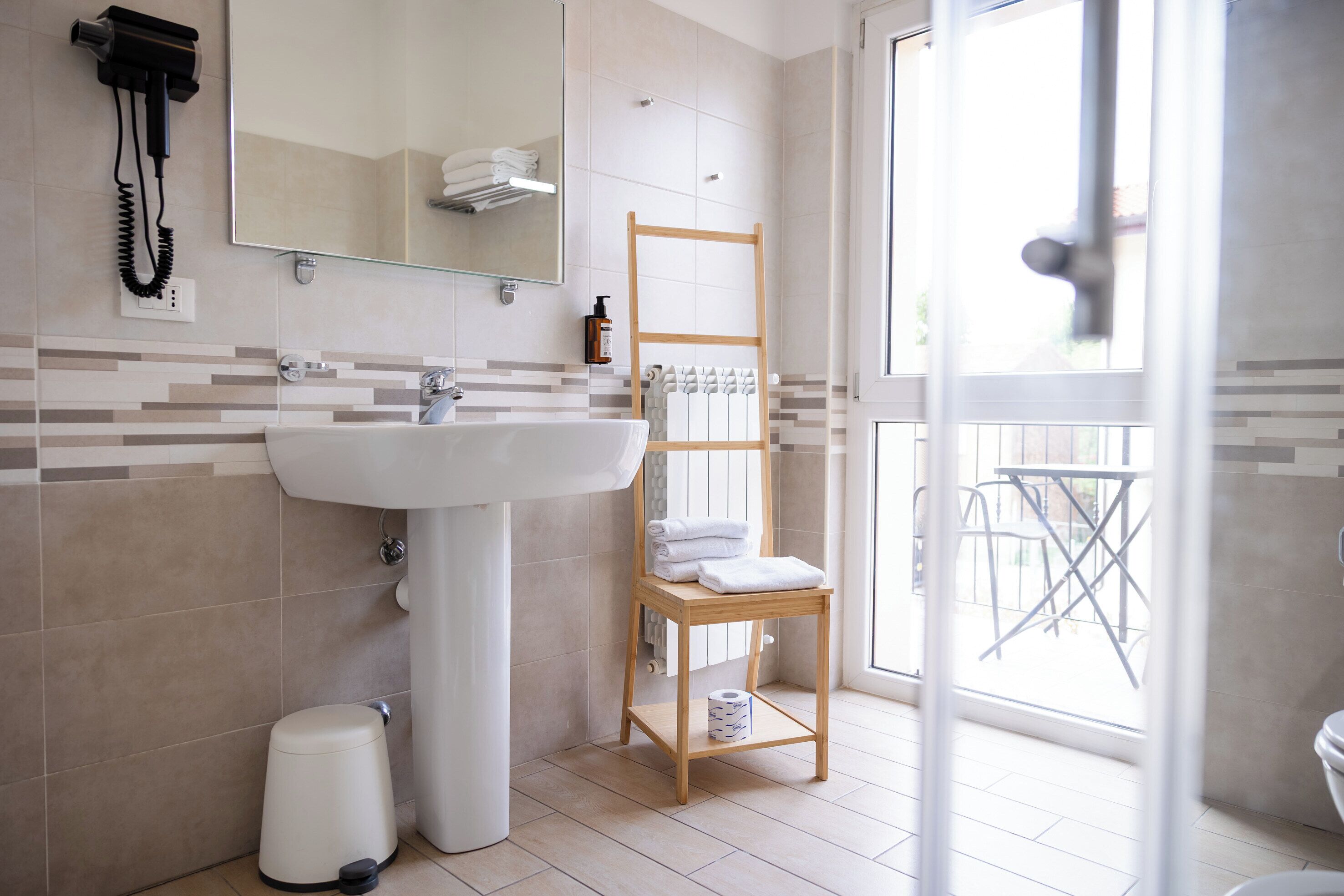 A bathroom with a sink, mirror, towel rack, and a window.