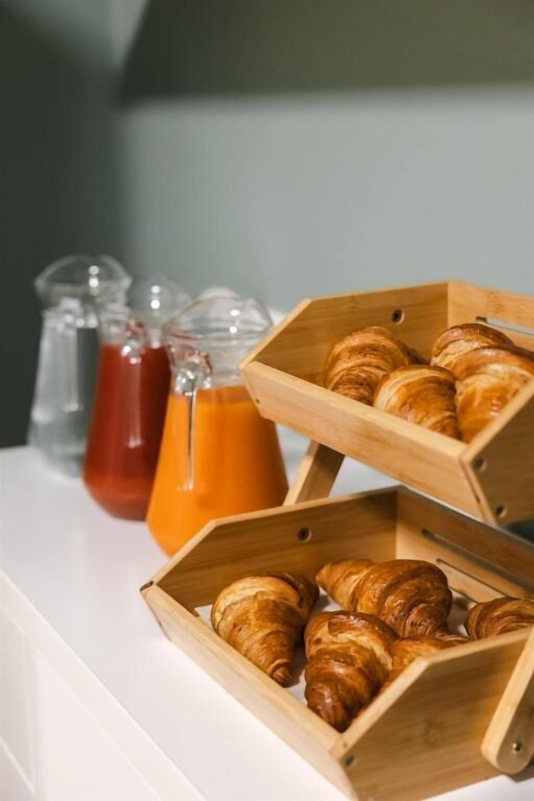 A breakfast setup with croissants in wooden boxes and two glass bottles of orange juice.