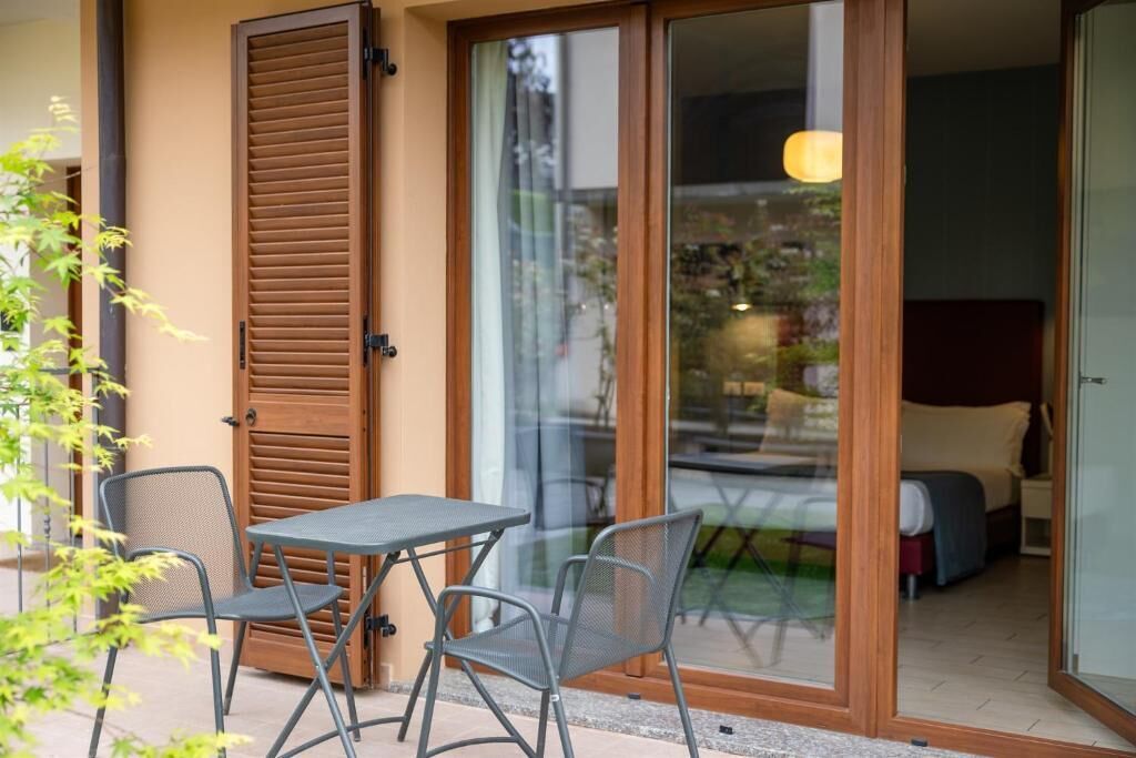 Quarto com porta de vidro deslizante, uma cama, mesa com cadeiras e vista para o exterior.