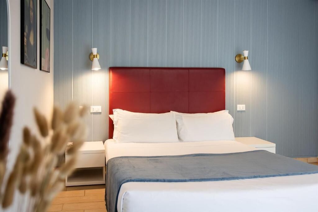 Una cama con cabecera roja, ropa de cama blanca y dos lámparas de noche.