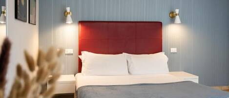 Una cama con cabecera roja, ropa de cama blanca y dos lámparas de noche.