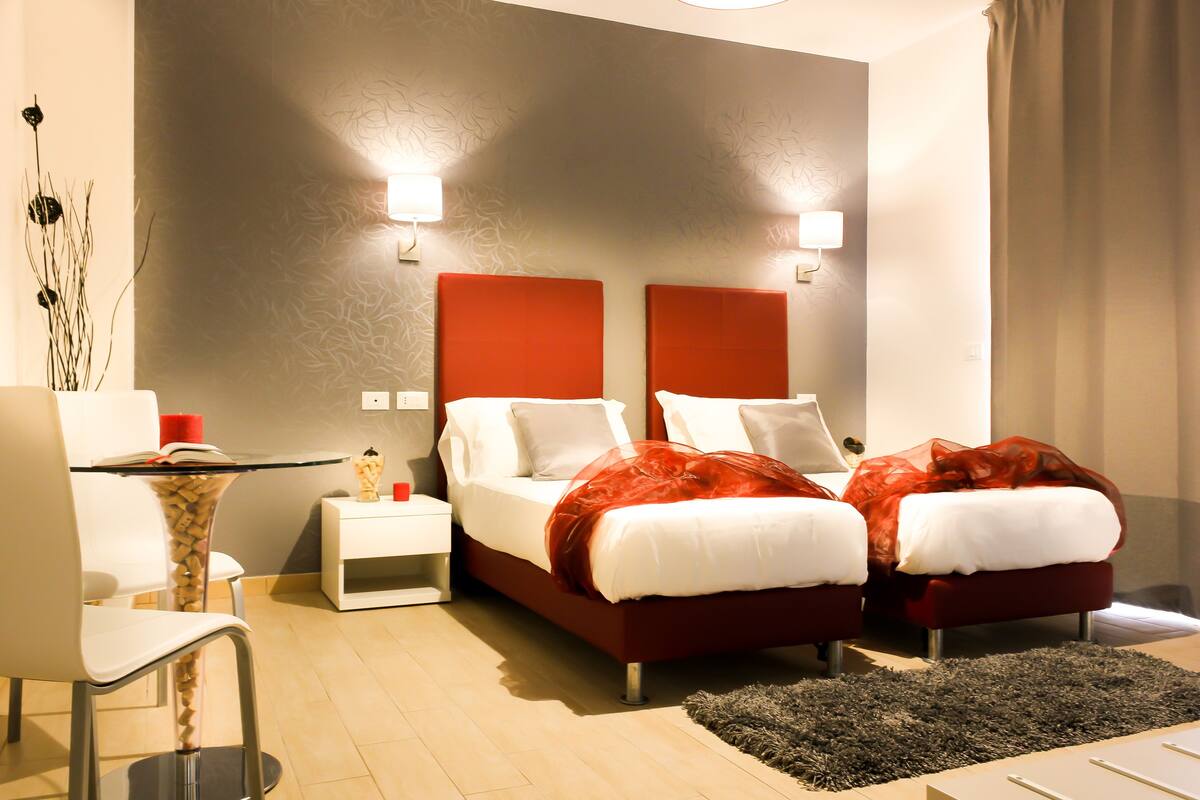 Una habitación de hotel moderna con dos camas, un escritorio con silla, una pequeña mesa con un florero y un adorno de pared.