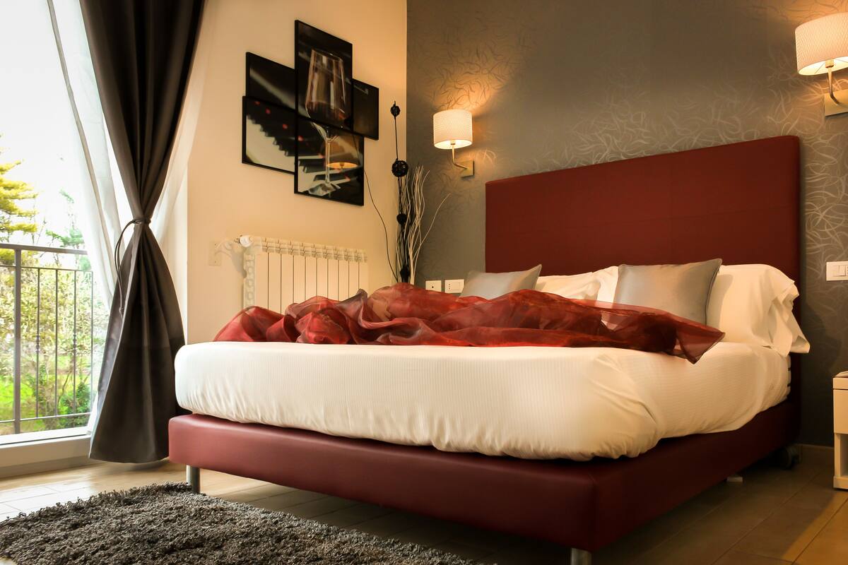 Un dormitorio moderno con cabecera roja, ropa de cama blanca y vistas al verdor exterior.