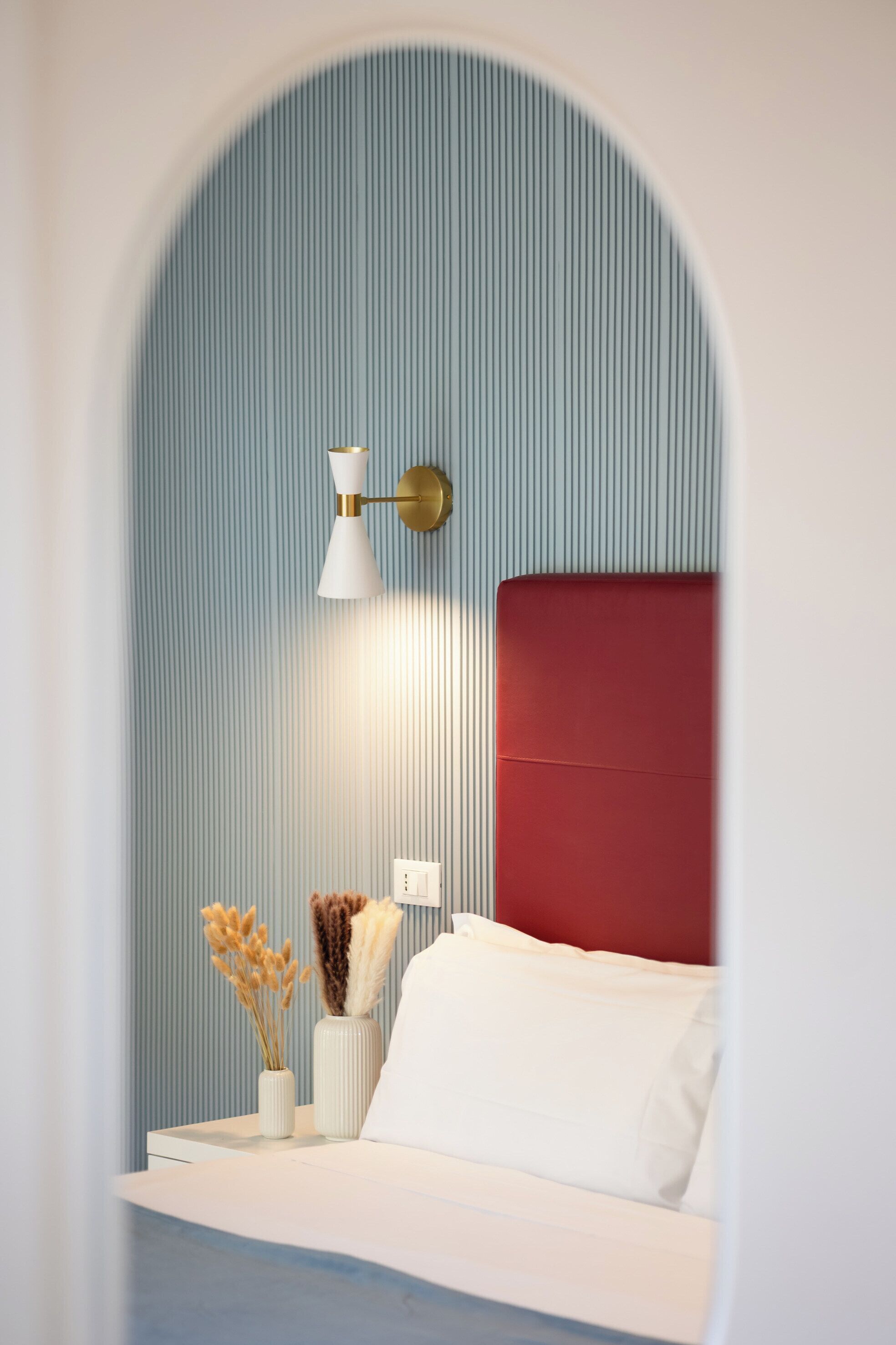 A bedroom with a red headboard, a bedside table with a lamp, and a wall with vertical lines.