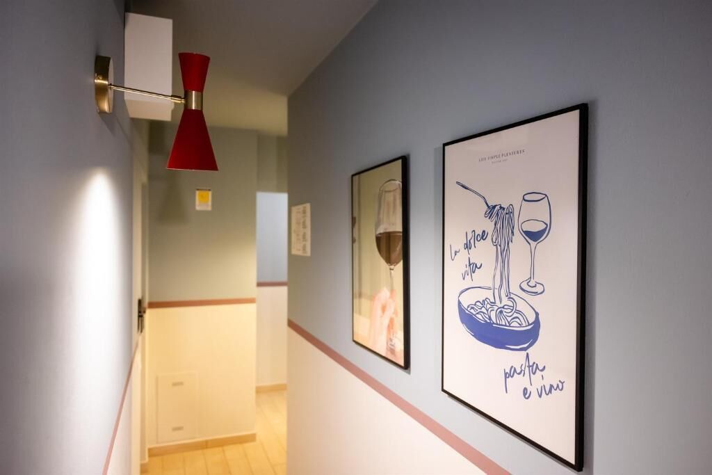 A hallway with framed artwork, a red pendant light, and a door leading to another room.