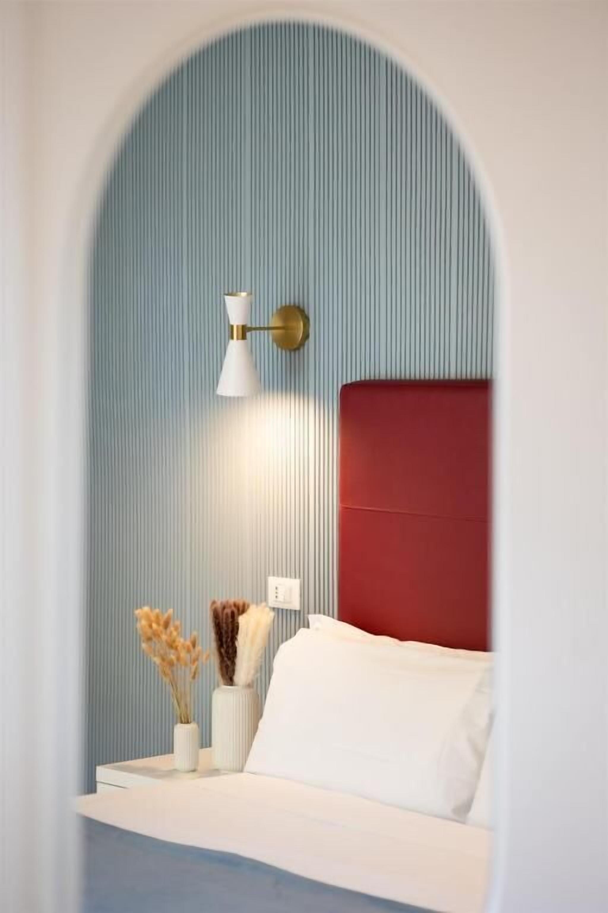 A bedroom with a red headboard, a white bedside table, and a wall-mounted lamp.