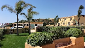 A residential area with a well-maintained lawn, palm trees, and a building with balconies. - Herons Bay Resort (Marsala)