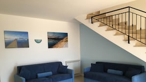 A living room with two blue sofas, a staircase with a black railing, and two landscape paintings on the wall. - Herons Bay Resort (Marsala)