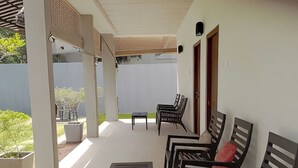 A covered outdoor seating area with a table and chairs, a small table with fruits, and a view of the garden. - Avita Holiday Home (Hikkaduwa)