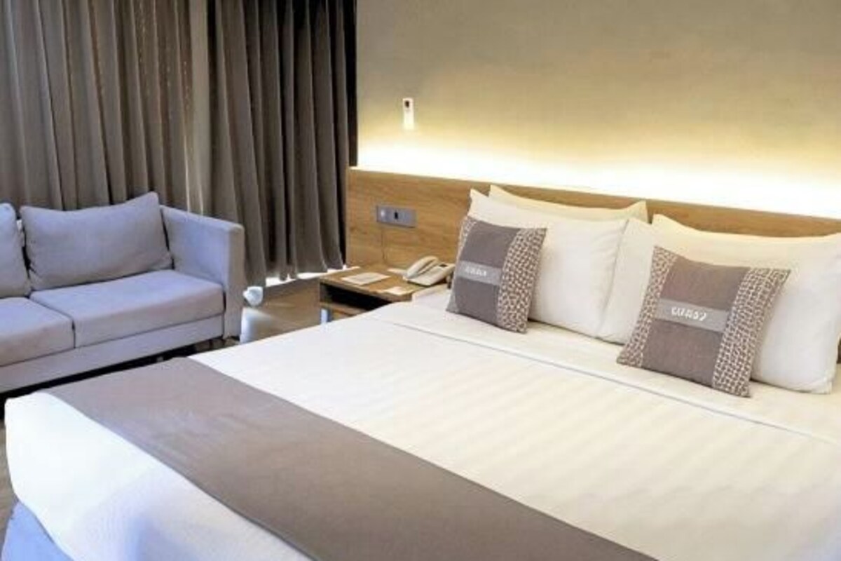 A hotel room with a large bed, a sofa, and a bedside table with a lamp.