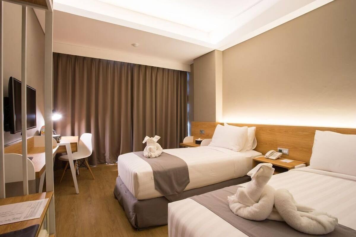 A hotel room with two beds, a desk, a chair, a TV, and a curtain.