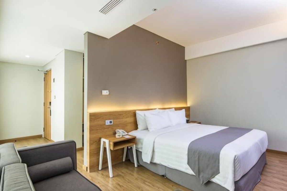 A hotel room with a bed, bedside table, and a small seating area.