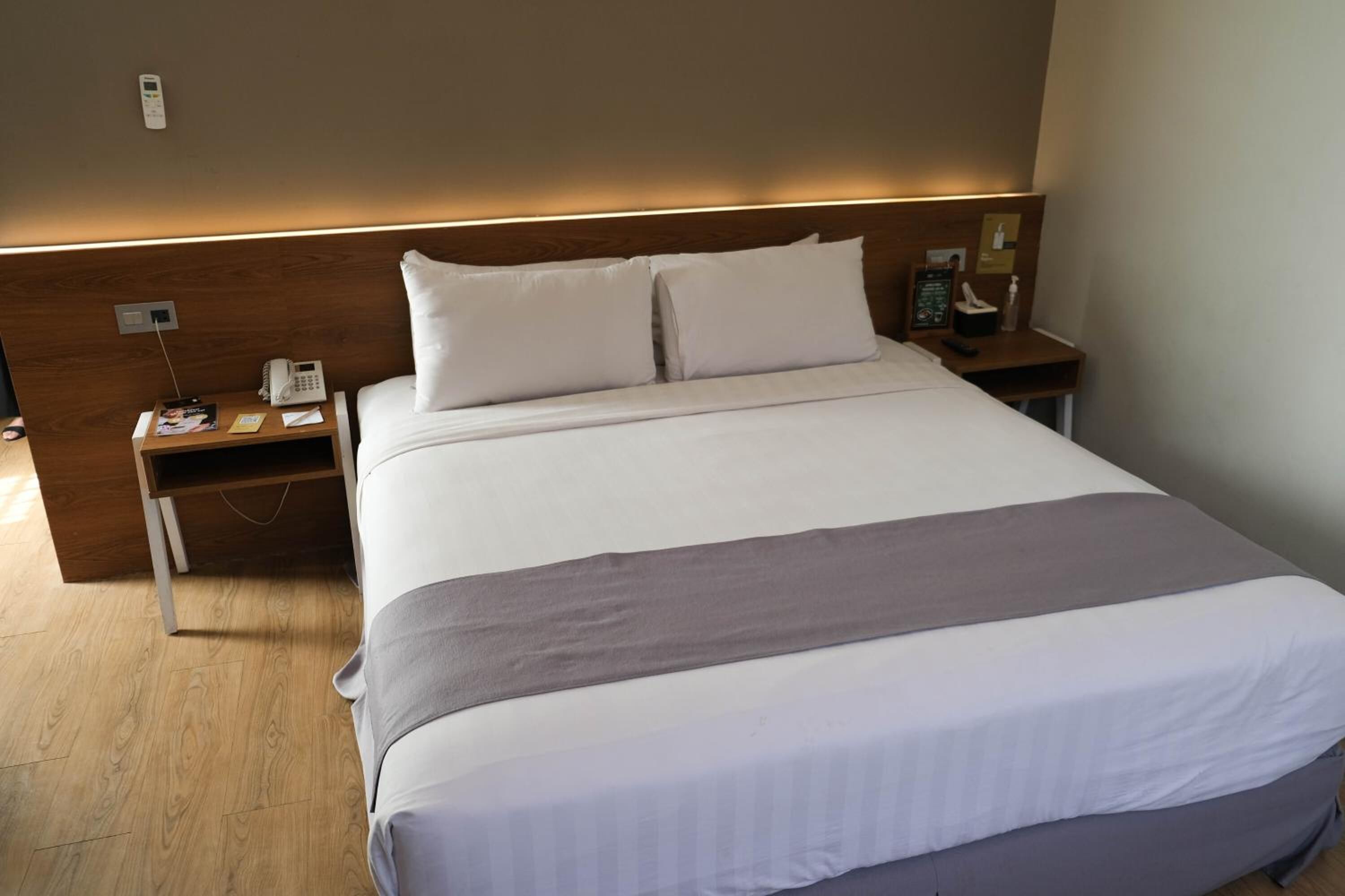Una habitación de hotel con una cama grande, un cabecero de madera, una mesita de noche con un teléfono y una lámpara, y otra mesita de noche con una lámpara.