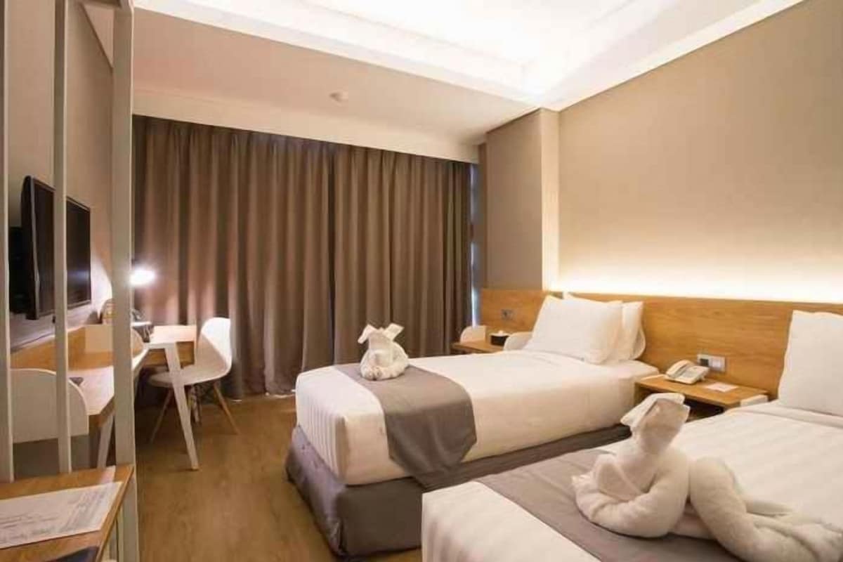 A hotel room with two beds, a desk, a chair, and a television.